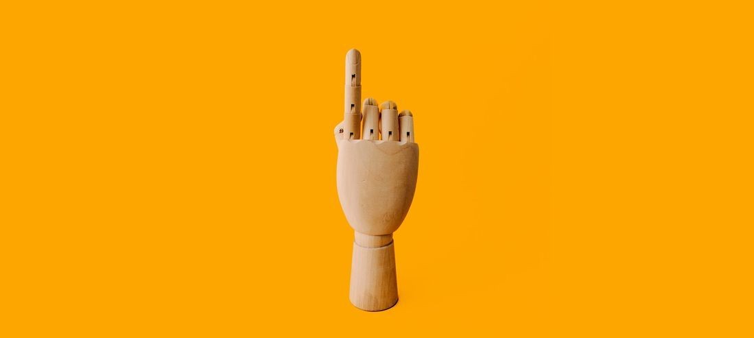 Wooden hand on yellow background pointing upwards